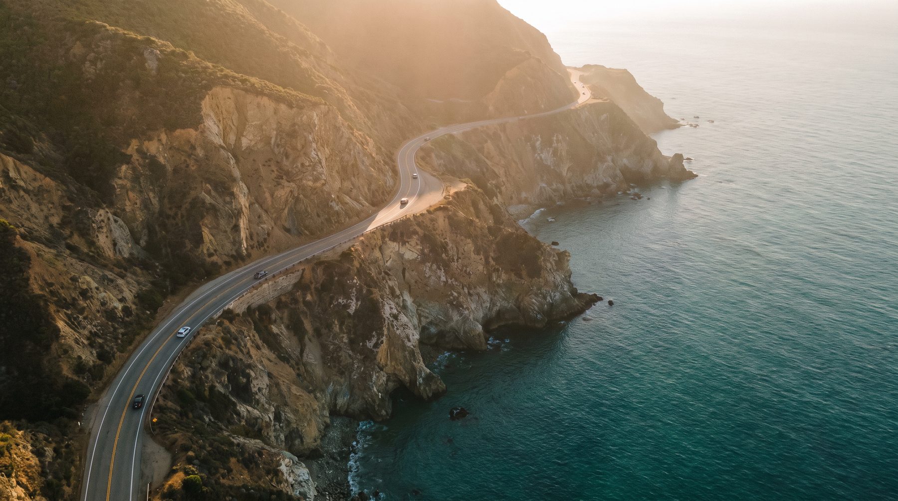 Aerial view of a California coastal highway curving above the Pacific at golden hour