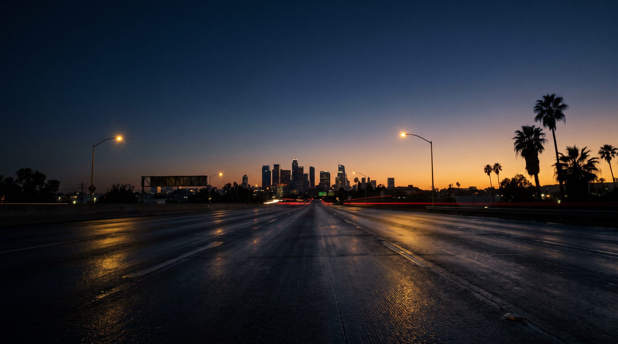 An empty California freeway at blue hour with the downtown skyline and palm trees on the horizon